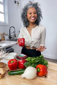 a woman sitting at a kitchen counter holding two red bell peppers and some green peppers