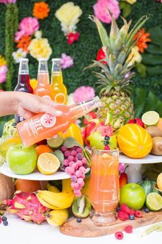 a person is pouring fruit juice into a glass on a plate with other fruits and flowers in the background