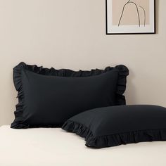 two black ruffled pillows sitting on top of a bed next to a framed painting