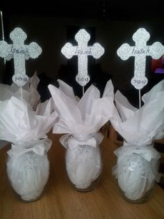 three mason jars filled with white paper bags and decorated crosses on top of them, sitting on a table