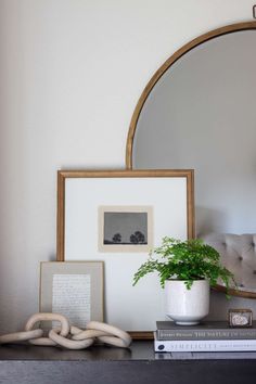 a table with a mirror, plant and pictures on it in front of a couch