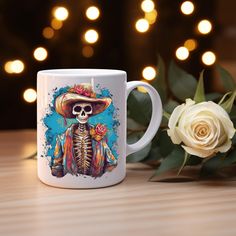 a white coffee mug with a skeleton wearing a sombrero and holding a rose