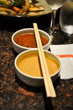 two bowls of soup and chopsticks on a table next to a glass of wine