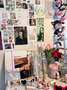 a table topped with lots of pink flowers next to a wall covered in pictures and photos