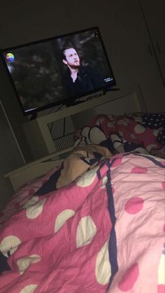 a television that is on in the corner of a room with a pink bedspread