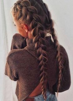 a girl with long braids in her hair wearing a brown sweater and jeans, looking out the window