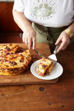 a person cutting into a pizza on top of a wooden table next to a white plate