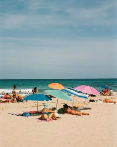 many people are laying on the beach under umbrellas