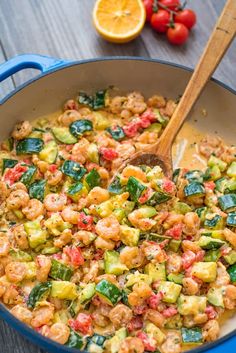 a skillet filled with shrimp, zucchini and tomatoes next to sliced oranges