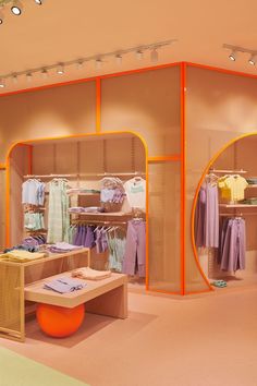 an orange and yellow clothing store display with clothes on hangers, tables and stools