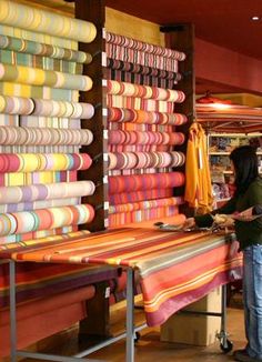 a woman standing next to a table covered in colorful fabrics