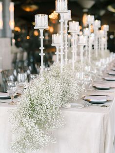 a long table with white flowers and candles on it is set for a formal dinner