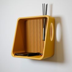 a yellow shelf with two black sticks sticking out of it's sides and a pen holder on the wall