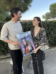 a man and woman standing next to each other holding up a framed photo with an image of the same person on it