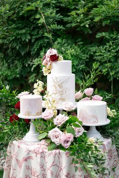 a three tiered wedding cake sitting on top of a table surrounded by greenery