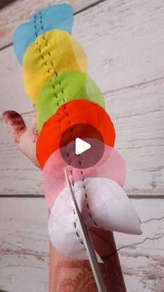 a person holding up a bunch of colorful pieces of fabric with scissors in their hand