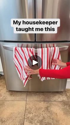 a woman holding a red and white striped towel in front of a stainless steel refrigerator