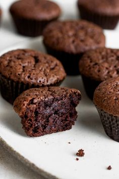 several chocolate muffins on a white plate with one cut in half and the other partially eaten