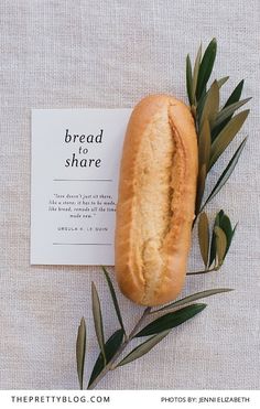 bread and olive leaves on top of a white table cloth with a card reading bread share