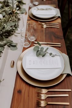 the table is set with plates, silverware and greenery