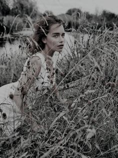 a woman sitting in tall grass next to a body of water