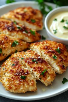 three pieces of chicken on a white plate with ranch dip and parsley in the background