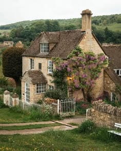 a stone house with purple flowers growing on it's roof and fenced in yard