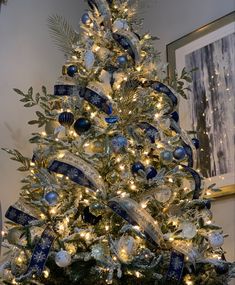 a decorated christmas tree with blue and white ribbons on it's branches, surrounded by lights