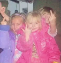 three children are posing for the camera with their fingers in the air and one girl is holding her hand up