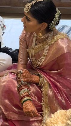 a woman sitting on top of a bed wearing a pink sari and gold jewelry