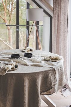 the table is set with two black plates and napkins on it, near an open window