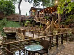 a wooden deck with chairs and tables next to a small pond in front of a house