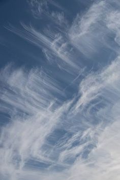 the airplane is flying high in the sky with some wispy clouds behind it