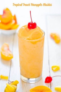 a pineapple slushie in a glass with a cherry on the top and yellow slices around it