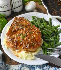 a white plate topped with meat and mashed potatoes covered in gravy next to green beans