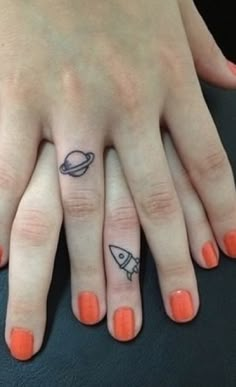 two fingers with small tattoos on them, one has a rocket and the other has a saturn tattoo