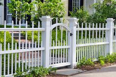 a white picket fence in front of a house with trees and bushes around the perimeter