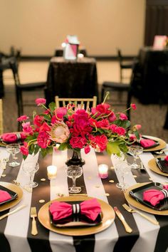 a black and white striped table cloth with pink flowers in a vase on the center