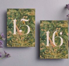 two cards with numbers on them next to some purple and green flowers in front of a gray background