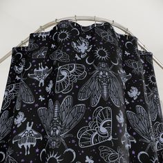 a black and white shower curtain with moths on it's side, hanging from a metal rod