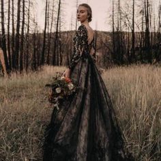 a woman standing in a field wearing a black dress