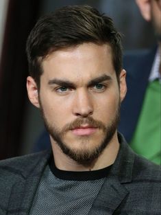 a close up of a man with a beard wearing a suit and green tie, looking at the camera