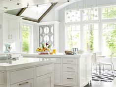 a kitchen with white cabinets and an island in front of two windows that look out onto the woods