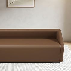 a brown leather couch sitting on top of a white rug in front of a painting