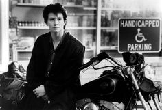 a man standing next to a parked motorcycle in front of a parking sign and store