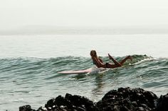 a woman laying on a surfboard in the ocean next to some rocks and water