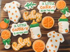 baby shower cookies decorated with oranges and green leaves on a wooden board, including ones that say it's a little cuter is on the way