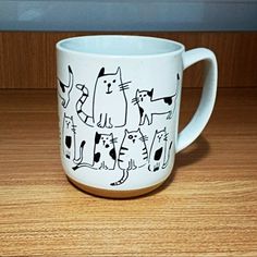 a white coffee mug with black cats on it sitting on a wooden countertop next to a window