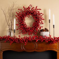 a fireplace mantel decorated with red berries and candles