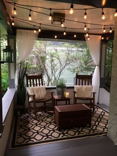 an outdoor living room with lights strung from the ceiling and wooden furniture set on top of a rug